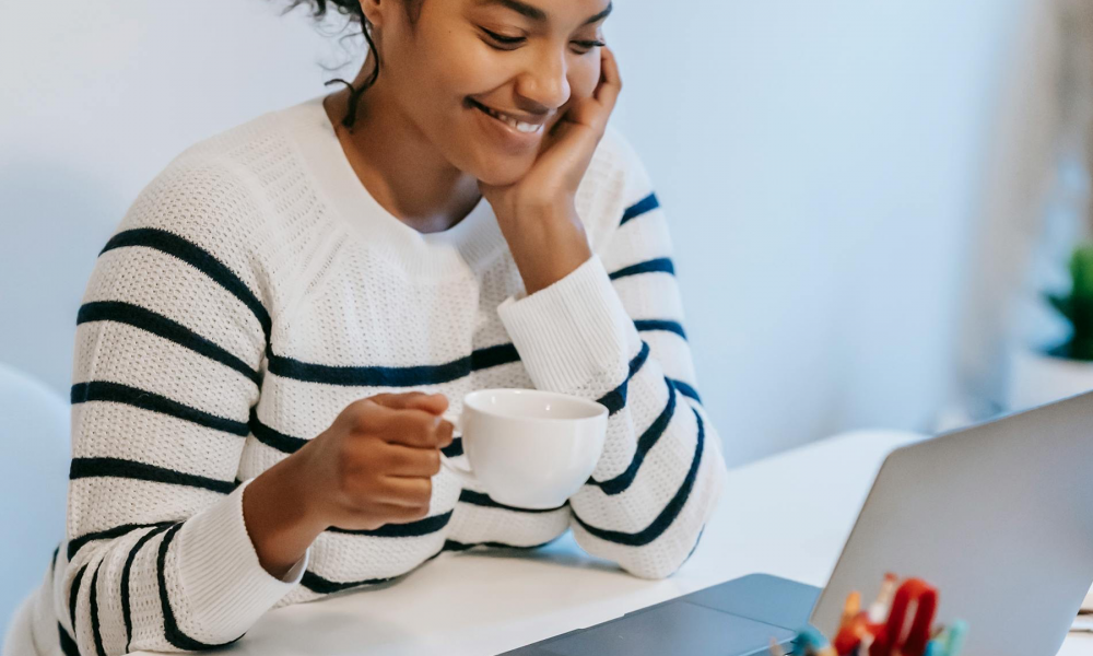 Young Woman Drinking Coffee And Using A Laptop Aspect Ratio 1000 600